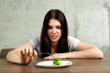 Anoreksiya Nervoza ya da küçük yeşil sebze plaka üzerinde sahip bulimia ile ilgili üzgün genç esmer kadın. Diyet sorunları, yeme bozukluğu.