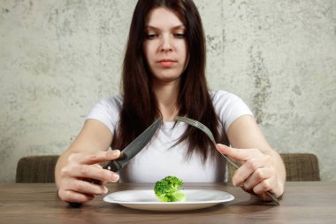 Anoreksiya Nervoza ya da küçük yeşil sebze plaka üzerinde sahip bulimia ile ilgili üzgün genç esmer kadın. Diyet sorunları, yeme bozukluğu.
