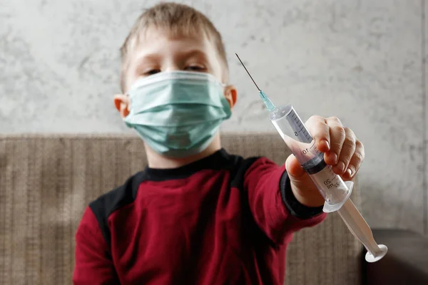 一个男孩的肖像, 一个戴着口罩的孩子, 手里拿着一把注射器。疾病的概念, 儿童的流感, 肺结核, 免疫力, 疾病的保护. — 图库照片