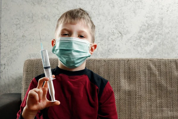 一个男孩的肖像, 一个戴着口罩的孩子, 手里拿着一把注射器。疾病的概念, 儿童的流感, 肺结核, 免疫力, 疾病的保护. — 图库照片