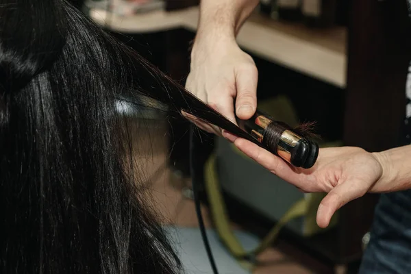 Close-up de mãos estilistas com ferro styling alisamento cabelo da mulher no salão — Fotografia de Stock