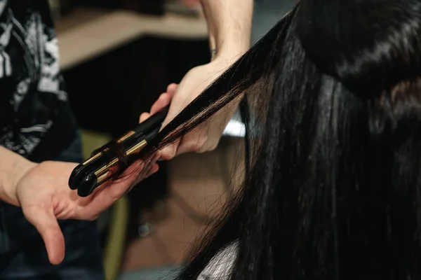 Close-up de mãos estilistas com ferro styling alisamento cabelo da mulher no salão — Fotografia de Stock