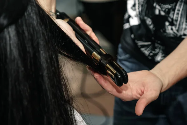 Close-up de mãos estilistas com ferro styling alisamento cabelo da mulher no salão — Fotografia de Stock