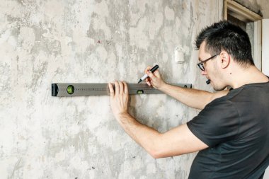 Bir adam önlemler bir cetvel, bir mezura, bir düzey duvar üzerinde veri işaretleyicilerini işaretler. Kavram inşaat çalışmalarını iş bitirme kendi elleriyle tamir.