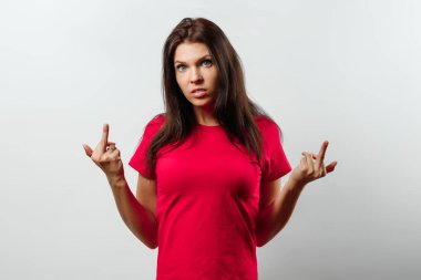 Orta parmak gösterilen genç güzeller güzeli bir kız. Hafif bir arka plan üzerinde izole. Farklı insan duyguları, yüz ifadesi, tutum, algı, beden dili, tepki duyguları.