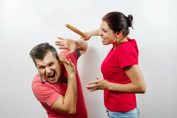 Family quarrel, wife scolds her husband, young, beautiful wife beats her husband with a stick. The concept of the psychology of family relations, marriage, domestic conflicts, domestic violence.
