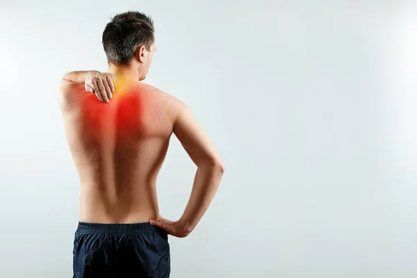 Ein Mann hält seine Hände für eine lädierte Schulter, ein Schmerz in der Schulter, der rot hervorgehoben ist. heller Hintergrund. das Konzept der Medizin. — Stockfoto