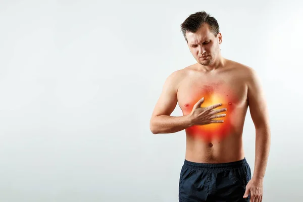 Un hombre sostiene sus manos y región del corazón, dolor en el pecho, un dolor en el corazón resaltado en rojo, un ataque al corazón. Fondo claro. El concepto de medicina, masaje, fisioterapia, salud . —  Fotos de Stock