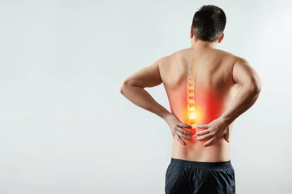 Achteraanzicht, de man heeft zijn handen achter zijn rug, pijn in de rug, pijn in de rug, in het rood gemarkeerd. Lichte achtergrond. Het concept van geneeskunde, fysiotherapie, massage en gezondheid. — Stockfoto