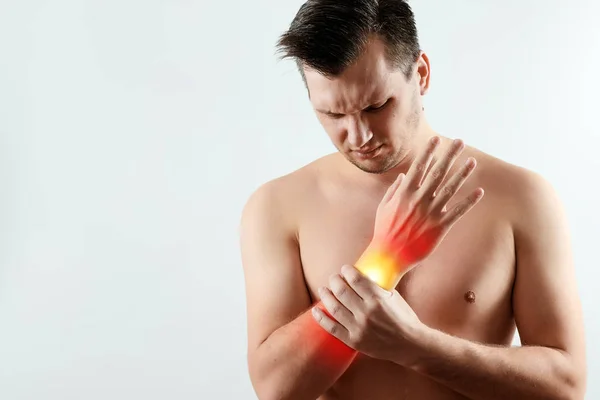 El hombre sostiene su muñeca, el dolor en su mano se destaca en rojo, el síndrome del túnel. Fondo claro. El concepto de medicina, masaje, fisioterapia, salud . —  Fotos de Stock