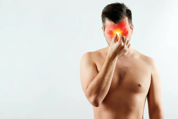 A man clings to the bridge of the nose, a headache highlighted in red, migraine. Light background. The concept of medicine, massage, physiotherapy, health. — Stock Photo, Image