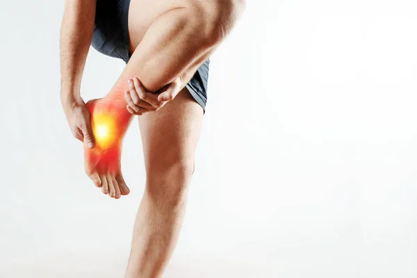 O homem segura as mãos no tornozelo, a dor na perna, a dor no pé é destacada em vermelho. Fundo claro. O conceito de medicina, massagem, fisioterapia, saúde . — Fotografia de Stock