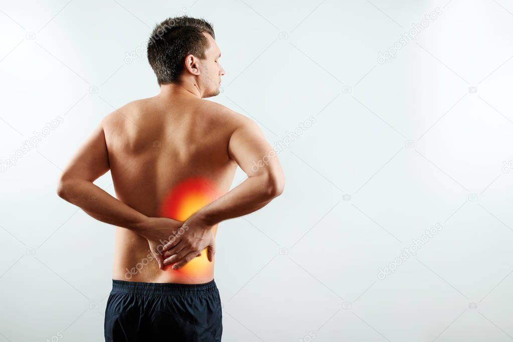 The man holds his hands behind his back, pain in the kidneys, pain in his back. Light background. The concept of medicine.