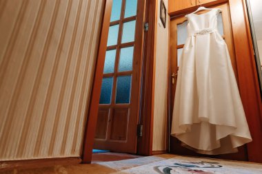 Bir kapı aralığında bir odada kahverengi bir arka plan üzerinde asılı bir gelinlik. Aile, evlilik, tatil, kutlama, Düğün.