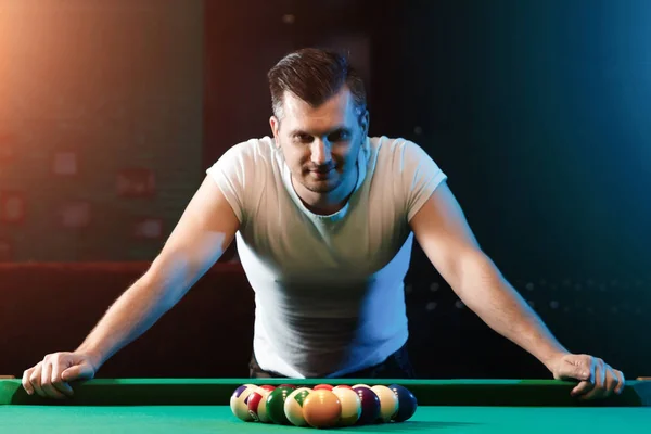 Un uomo con una maglietta bianca sta giocando a biliardo, uno sfondo scuro. Piacevole passatempo, intrattenimento, tempo libero, vacanze in famiglia, giochi. — Foto Stock