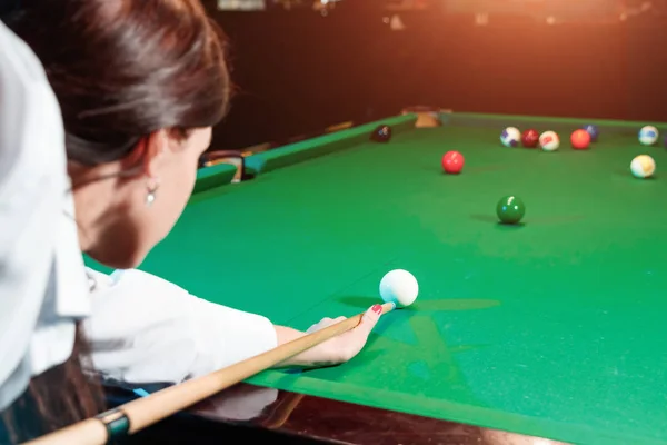 Jong mooi meisje speelt biljart. Donkere achtergrond. Aangenaam tijdverdrijf, rust, vermaak. — Stockfoto