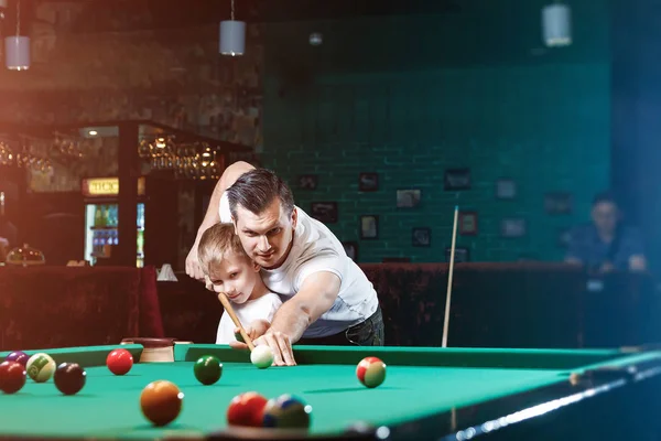 Padre e figlio giocano a biliardo. Il padre insegna a suo figlio a giocare a biliardo. Il concetto di genitori e figli, educazione, riposo familiare . — Foto Stock