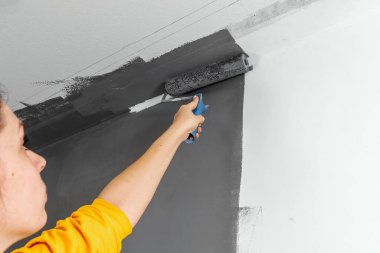 Sarı kazaklı güzel bir kız gri boyayla bir duvar boyuyor. Oda boyama, onarım, tasarım. Boşluğu kopyala.