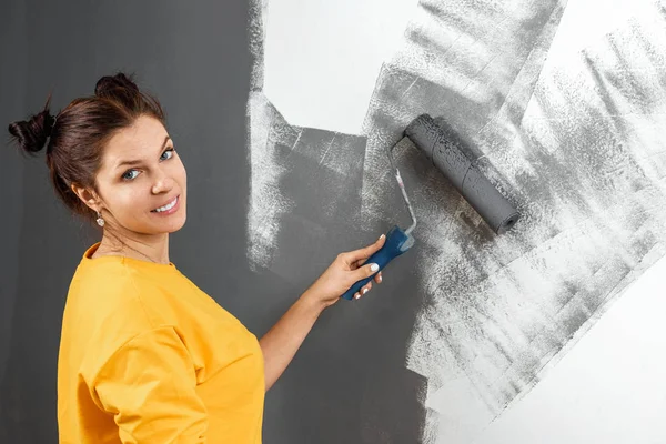 A bela menina em um suéter amarelo pinta uma parede na pintura cinza. Pintura, reparação, design. Espaço de cópia . — Fotografia de Stock