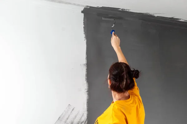 A bela menina em um suéter amarelo pinta uma parede na pintura cinza. Pintura, reparação, design. Espaço de cópia . — Fotografia de Stock