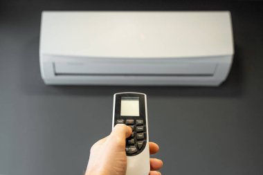 Gri bir duvardaki beyaz klimanın arka planında, klimanın uzaktan kumandası var. Sıcaklık, serinlik, serinlik, tazelik kavramı..