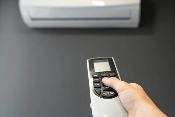 Mano con telecomando da un condizionatore d'aria primo piano su uno sfondo di un condizionatore d'aria bianco su una parete grigia. Il concetto di calore, aria fresca, raffreddamento, freschezza . — Foto Stock