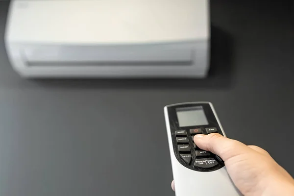 Mano con telecomando da un condizionatore d'aria primo piano su uno sfondo di un condizionatore d'aria bianco su una parete grigia. Il concetto di calore, aria fresca, raffreddamento, freschezza . — Foto Stock