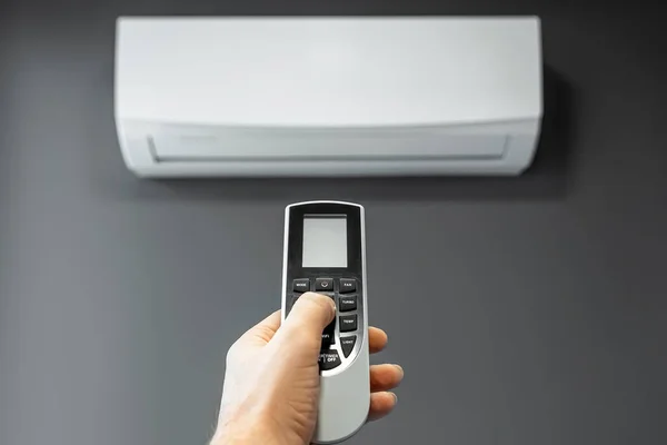 Mano con telecomando da un condizionatore d'aria primo piano su uno sfondo di un condizionatore d'aria bianco su una parete grigia. Il concetto di calore, aria fresca, raffreddamento, freschezza . — Foto Stock