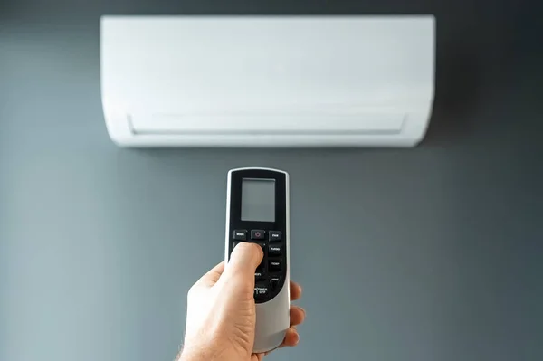 Hand with a remote control from an air conditioner close-up on a background of a white air conditioner on a gray wall. The concept of heat, cool air, cooling, freshness.