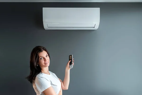 Una hermosa chica está bajo el aire acondicionado y una corriente de aire fresco y frío contra una pared gris. El concepto de calor, aire fresco, enfriamiento, frescura . —  Fotos de Stock