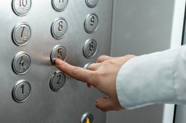 Kadın eli, parmak asansör düğmesine basar. Kariyer basamaklarını çık.