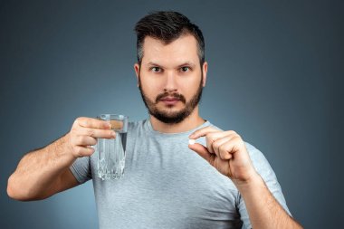 Bir adam elinde bir bardak su ve hap tutuyor, ilaç alıyor, tedavi oluyor, geçmişi gri. Tıbbi tema, vitaminler, sağlık hizmetleri.