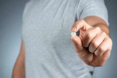 Erkek eli beyaz bir hap tutuyor, ilaç alıyor, tedavi görüyor, geçmişi gri. Tıbbi tema, vitaminler, sağlık hizmetleri.