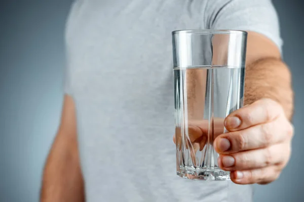 Szklany kubek z czystej wody mineralnej w męskich rękach zbliżenie na szarym tle. leki, leczenie, zdrowy napój. — Zdjęcie stockowe
