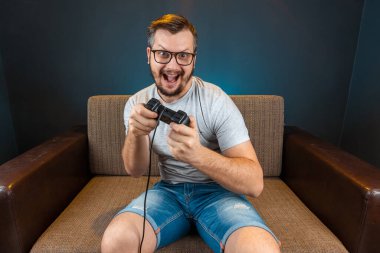 A man plays the console, video games react strongly and emotionally while sitting on the couch. Day off, entertainment, leisure.