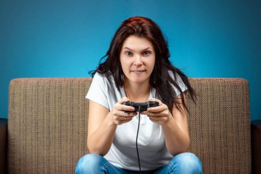 A cheerful girl plays on the console, in video games, emotionally react while sitting on the couch. Day off, entertainment, leisure.