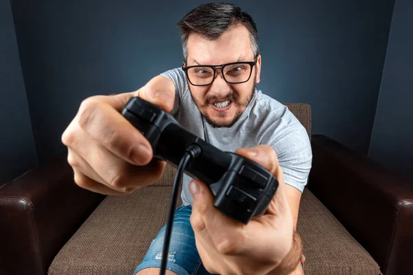 Un homme joue de la console, les jeux vidéo réagissent fortement et émotionnellement tout en étant assis sur le canapé. Jour de repos, divertissement, loisirs . — Photo