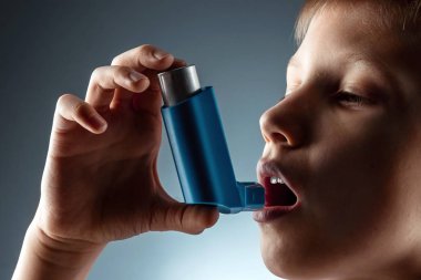 Portrait of a boy using an asthma inhaler to treat inflammatory diseases, shortness of breath. The concept of treatment for cough, allergies, respiratory tract disease.