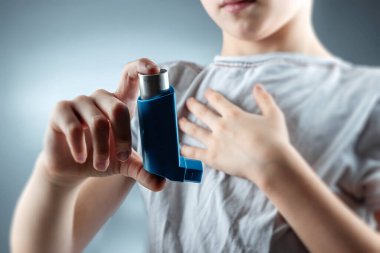The boy holds an asthma inhaler in his hands to treat inflammatory diseases, shortness of breath. The concept of treatment for cough, allergies, respiratory tract disease.