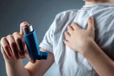 The boy holds an asthma inhaler in his hands to treat inflammatory diseases, shortness of breath. The concept of treatment for cough, allergies, respiratory tract disease.