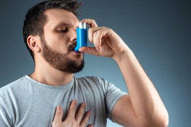 Portrait of a man with an asthma inhaler in his hands, an asthmatic attack. The concept of treatment of bronchial asthma, cough, allergies, dyspnea.