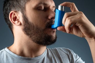 Portrait of a man with an asthma inhaler in his hands, an asthmatic attack. The concept of treatment of bronchial asthma, cough, allergies, dyspnea. clipart