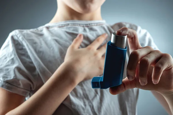 The boy holds an asthma inhaler in his hands to treat inflammatory diseases, shortness of breath. The concept of treatment for cough, allergies, respiratory tract disease.