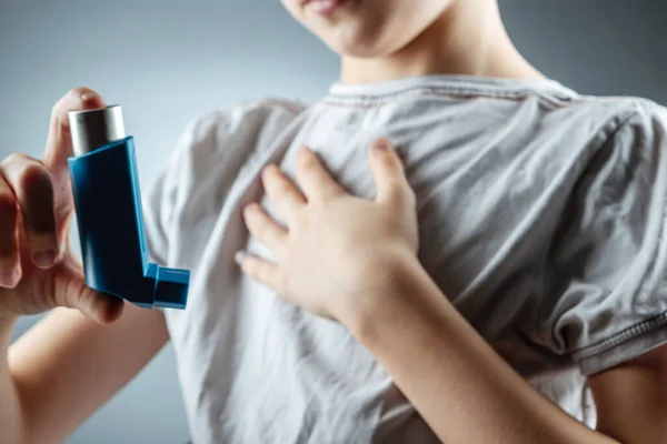 O menino segura um inalador de asma em suas mãos para tratar doenças inflamatórias, falta de ar. O conceito de tratamento para a tosse, alergias, doença do trato respiratório . — Fotografia de Stock