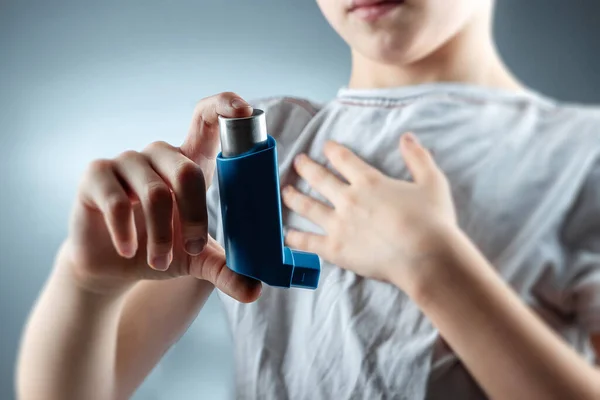 Il ragazzo tiene in mano un inalatore per l'asma per curare malattie infiammatorie, mancanza di respiro. Il concetto di trattamento per tosse, allergie, malattie delle vie respiratorie . — Foto Stock