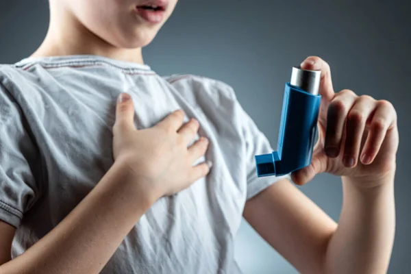 O menino segura um inalador de asma em suas mãos para tratar doenças inflamatórias, falta de ar. O conceito de tratamento para a tosse, alergias, doença do trato respiratório . — Fotografia de Stock