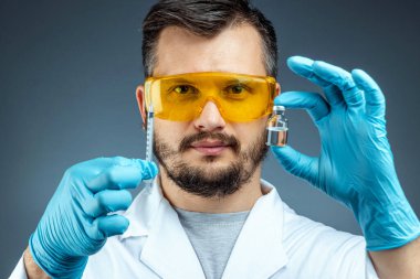 Male scientist, laboratory assistant in a white coat and glasses holds a bottle with a vaccine in his hands, medical tests, laboratory, experiments. Immunization chemical analysis.