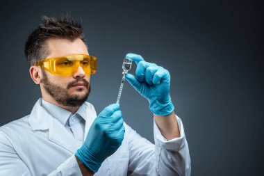 Male scientist, laboratory assistant in a white coat and glasses holds a bottle with a vaccine in his hands, medical tests, laboratory, experiments. Immunization chemical analysis.