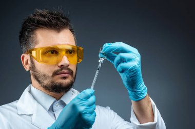 Male scientist, laboratory assistant in a white coat and glasses holds a bottle with a vaccine in his hands, medical tests, laboratory, experiments. Immunization chemical analysis.