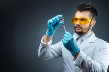 Male scientist, laboratory assistant in a white coat and glasses holds a bottle with a vaccine in his hands, medical tests, laboratory, experiments. Immunization chemical analysis.